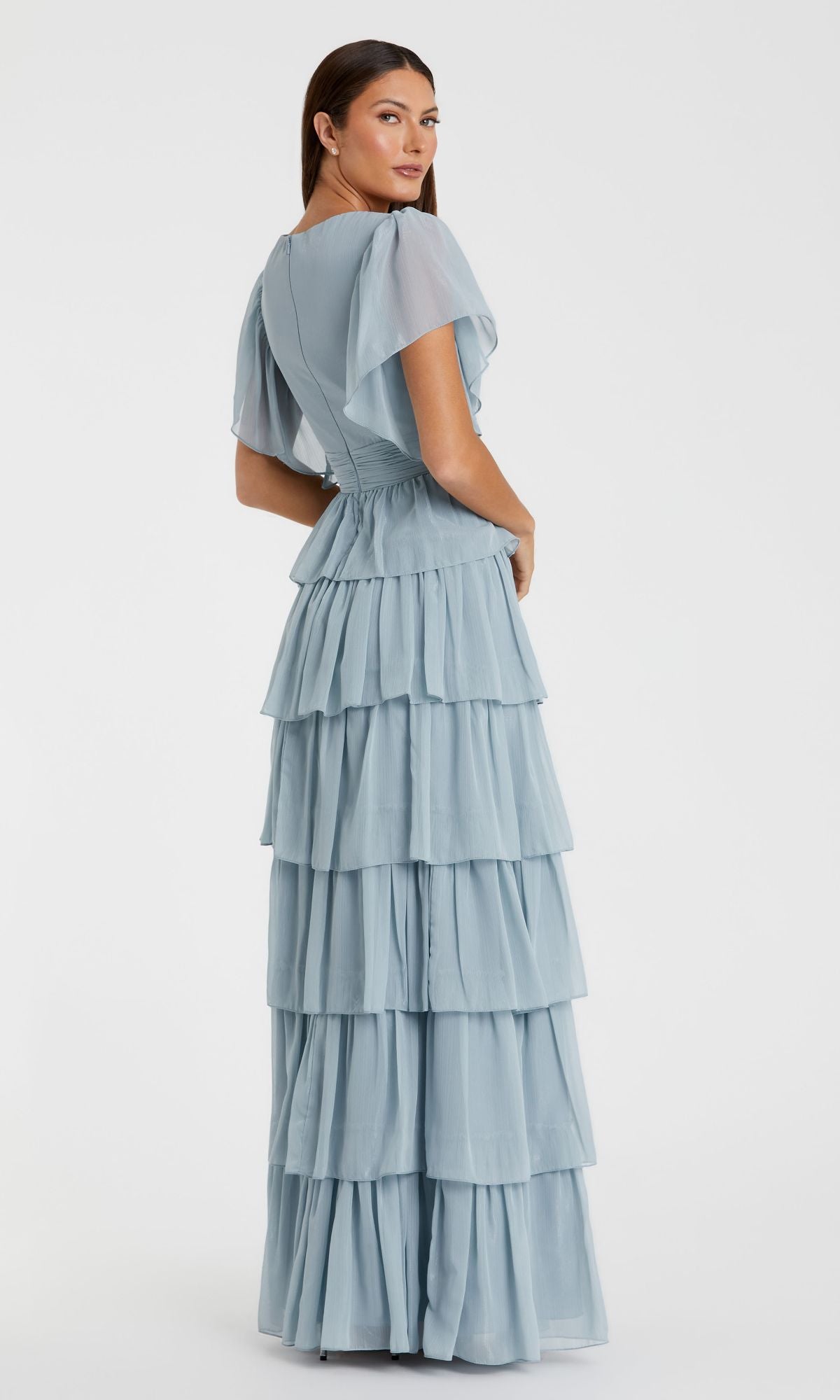 A woman faces away, wearing the Mac Duggal 49595 Flutter-Sleeve Long Formal Dress in light blue, featuring short flutter sleeves and ruffled tiered layers, set against a plain white background.